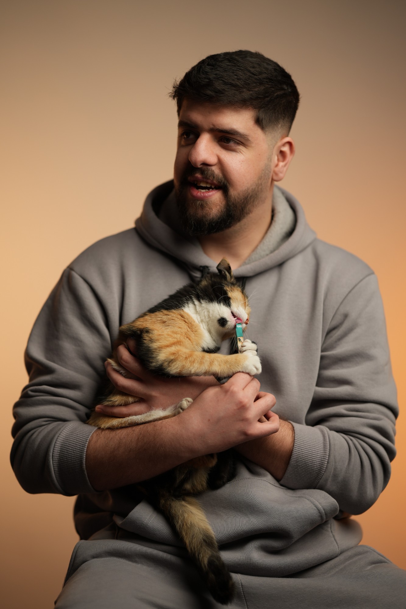 Hatem Hameed in a grey hoodie, holding a calico cat